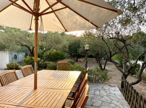 Schattiger Speiseterrasse unter Sonnenschirm mit Holztisch und Stühlen, Blick auf den Olivenhain von Villa Moka
