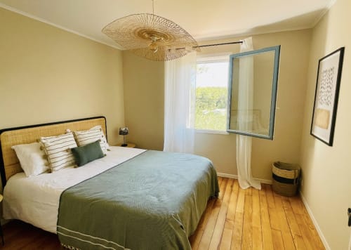 Helles Schlafzimmer in der Villa Moka der La Conciergerie De Franck mit gelben Wänden, Holzböden, Korbgeflecht-Kopfteil und Gartenblick