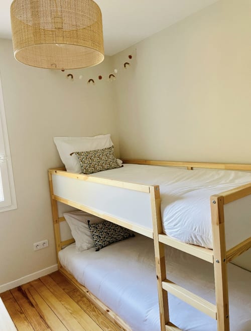 Etagenbett aus Holz mit weißer Bettwäsche im Schlafzimmer der Villa Moka, geflochtene Deckenleuchte, hellgelbe Wände