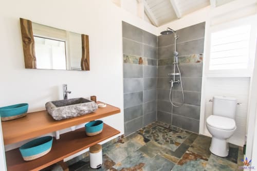 Modern bathroom at Le Domaine De L'ilet cottage with stone sink, walk-in shower, toilet, and wooden vanity with turquoise