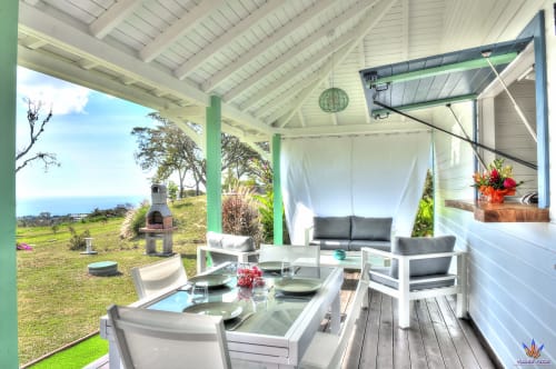 Covered patio with dining table, lounge seating, and ocean view at Kaz'Quisqualis cottage in Guadeloupe