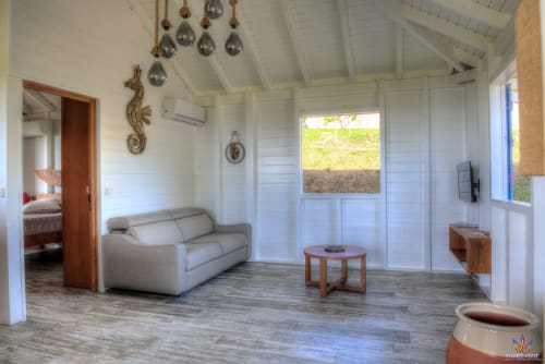 Bright cottage living room at Le Domaine De L'ilet with beige sofa, wooden furniture, and sea view windows in Saint-Claude,