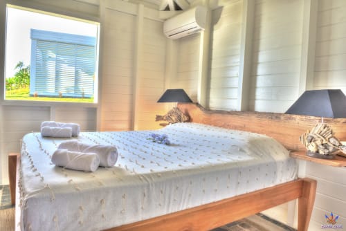 Bright cottage bedroom at Le Domaine De L'ilet with wooden bed, white bedding, sea view window, and AC unit in Saint-Claude