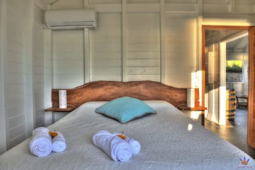 Kaz'Samana cottage bedroom at Le Domaine De L'ilet with wooden bed, blue pillow, rolled towels, AC unit, and sea views in