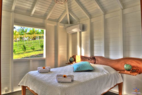 Bright cottage bedroom at Le Domaine De L'ilet with white walls, wooden bed frame, and garden view through window in