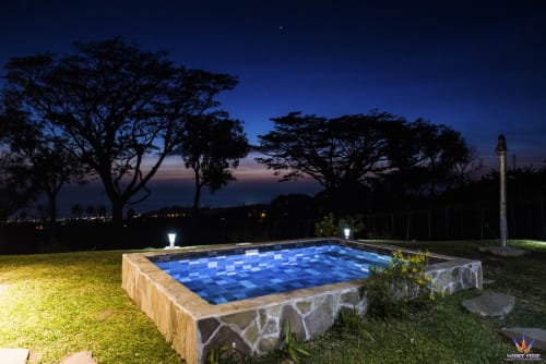 Illuminated swimming pool at dusk with blue tiles, stone edge, manicured lawn, and silhouetted trees at Le Domaine De L'ilet,