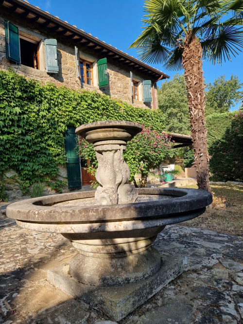 Stone urn fountain in Italian villa courtyard with ivy-covered historic building and palm tree