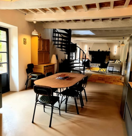 Modern villa dining area with wooden table, black chairs, spiral staircase, and open living space with fireplace