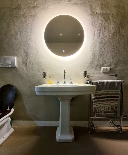 Modern bathroom at Villa Italia with pedestal sink, illuminated circular mirror, and heated towel rack against textured walls