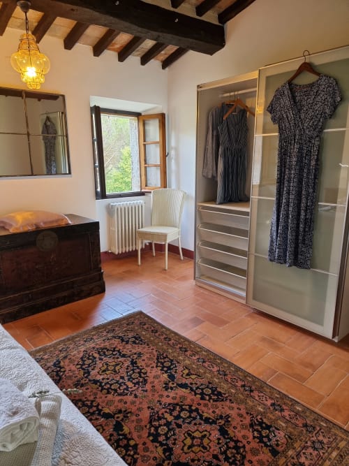 Spacious villa bedroom with wardrobe, terracotta floors, exposed beams, and garden views