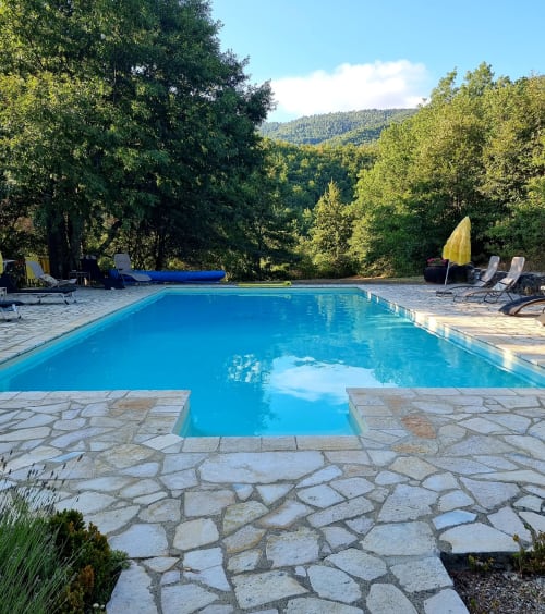 Sparkling resort pool surrounded by stone patio with lounge chairs and yellow umbrella, mountain forest backdrop