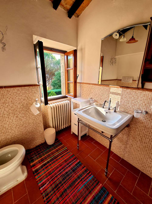 Spacious bathroom in Secret Villa with terracotta tiles, beige mosaic walls, vessel sink, and garden view through French
