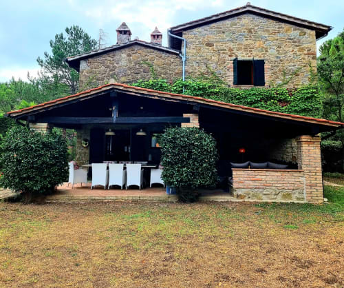 Modern villa with stone and brick architecture, covered patio with dining area, lush gardens, Italy