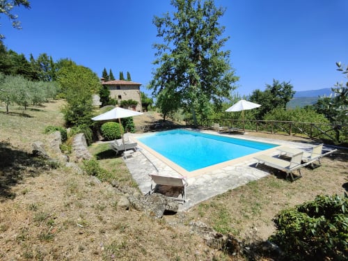 Tuscan villa with rectangular blue swimming pool, white umbrellas, lounge chairs, stone building, and cypress trees on