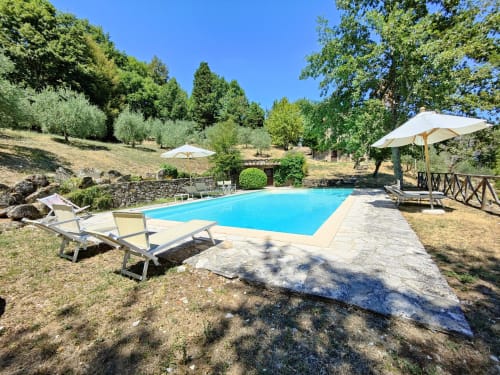 Tuscany villa pool with loungers, umbrellas, and olive trees under clear blue sky