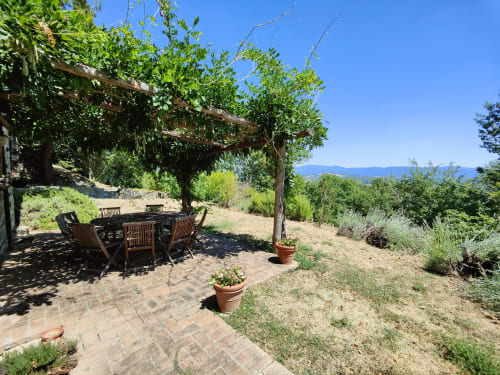 Tuscan villa pergola dining area with wooden chairs, terracotta pots, and mountain views