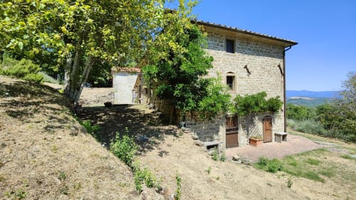 Rustic Italian stone villa with terracotta accents, surrounded by green vegetation and mountains in background
