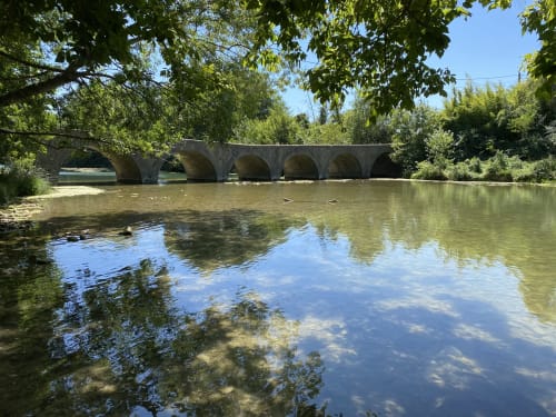 Pont de pierre historique enjambant une rivière calme, entouré d'arbres luxuriants près de La Conciergerie De Franck, Boissieres