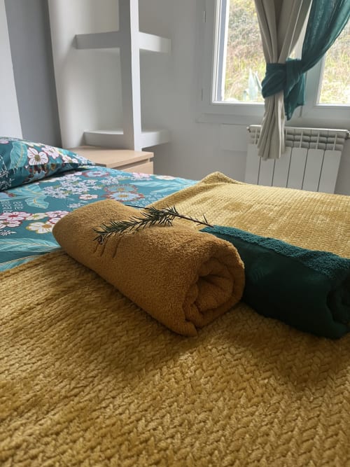 Aufgerolltes goldenes Handtuch mit Feder auf dem Bett in La Conciergerie De Franck, Boissieres