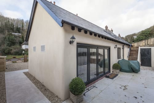 Cottage moderno a Three Little Pigs, Blandford Forum, con muri color crema, tetto scuro e porte-finestre che si affacciano sulla terrazza.
