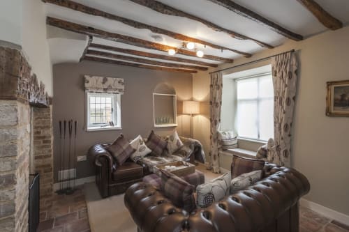 Accogliente lounge con travi a vista, divani in pelle, camino e tende a motivi presso Three Little Pigs, Blandford Forum