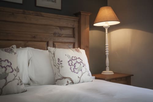 Accogliente camera dell'hotel Three Little Pigs a Blandford Forum con cuscini floreali, testata in legno e lampada da comodino