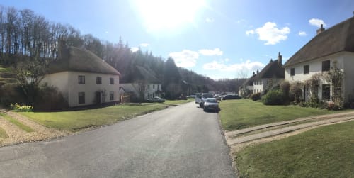I cottage con tetto di paglia dei Tre Porcellini nella strada del villaggio di Blandford Forum con prati verdi e auto parcheggiate