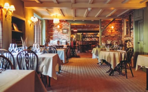 Elegant dining room at Three Little Pigs hotel in Blandford Forum with white tablecloths, black chairs, and brick walls.