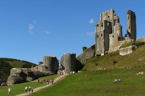 Corfe Castle ruins on green hillside near Blandford Forum, Dorset with visitors exploring historic stone towers and grounds