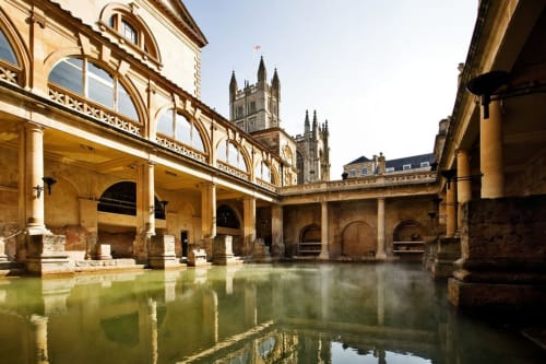 Roman Baths in Bath with stone columns and green thermal waters, Abbey church visible behind
