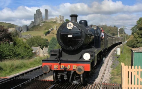 Steam locomotive 88 on tracks near Blandford Forum with historic castle ruins on hillside