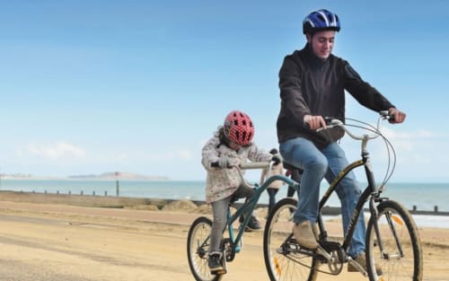 Adult and child cycling on beach near Blandford Forum with clear sky and sea view