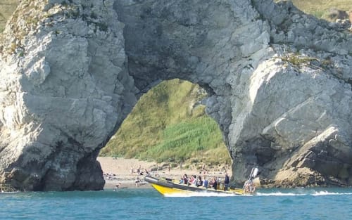 Yellow boat with tourists passing through natural rock arch near Blandford Forum coastal cliffs