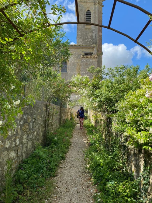 Overgrown garden path with white flowers leading to stone tower at Le Rêve d'Alice, Saint-Puy