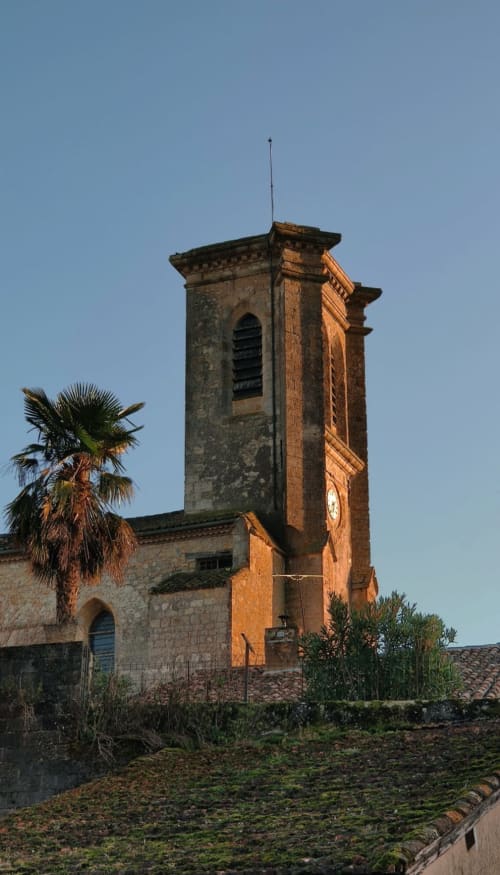 Historic bell tower at Le Rêve d'Alice, a charming B&B in Saint-Puy, France, with palm tree and clear blue sky