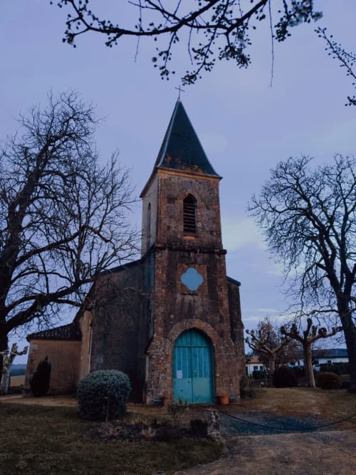 Historic stone church with turret and turquoise door at Le Rêve d'Alice B&B in Saint-Puy, France