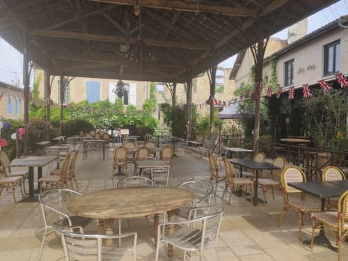 Le Rêve d'Alice courtyard patio with wooden tables, rattan chairs, and pergola in Saint-Puy