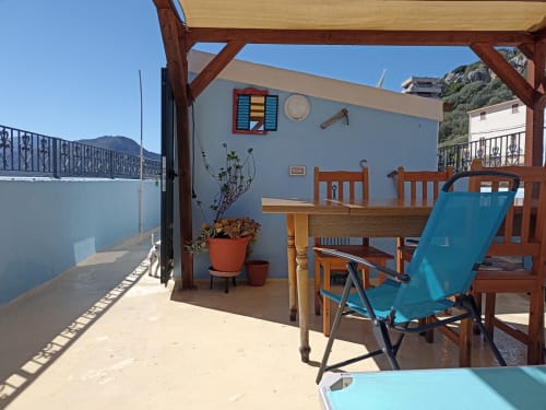 Sunny terrace at B&B Eleonora D'Arborea in Posada with wooden furniture, blue lounger, and mountain views