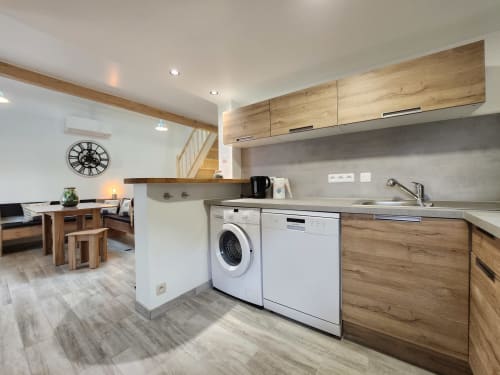 Modern cottage kitchen with wooden cabinets, washing machine, sink, and open-plan living area at Domaine à l'Aise