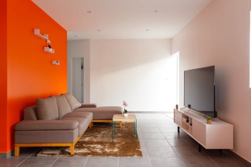 Salon moderne de la maison d'hôtes Kaz A Bibi à Sainte-Rose avec mur d'accent orange, canapé rose et télévision écran plat
