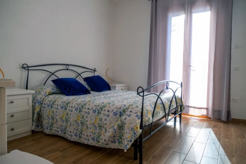 Camera luminosa a La Casetta di Pietra B&B a Gavorrano con letto in ferro battuto, cuscini blu e accesso al balcone