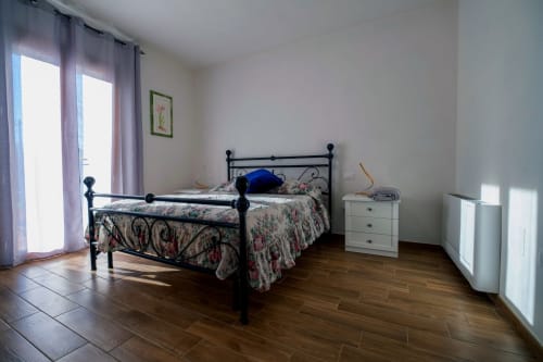 Spaziosa camera da letto con letto in ferro battuto nero, biancheria floreale, pavimenti in legno e porte finestre verso il balcone a La Casetta di Pietra
