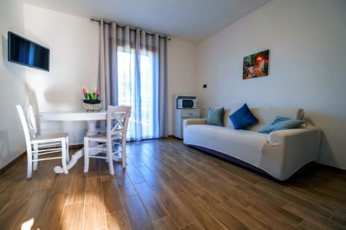 Moderna camera studio presso La Casetta di Pietra B&B a Gavorrano con arredamento bianco, divano, zona pranzo e balcone con vista sul giardino