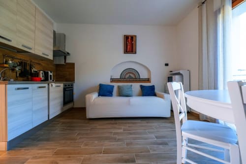 Sala open-plan moderna a La Casetta di Pietra a Gavorrano con divano bianco, cucina, zona pranzo e balcone con vista sul giardino