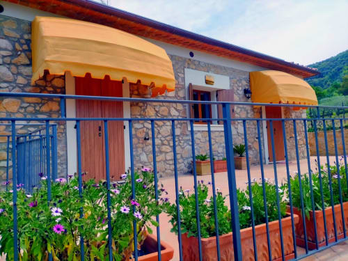 La Casetta di Pietra B&B a Gavorrano con muri in pietra, tende gialle, ringhiere blu e fiori viola sulla vista giardino