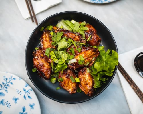Glazed chicken wings with green onions and cilantro in black bowl at La Conciergerie De Franck, Boissieres