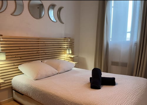 Modernes Hotelzimmer in der La Conciergerie De Franck mit Holzlattenrahmen, weißer Bettwäsche und mondförmiger Spiegeldekoration