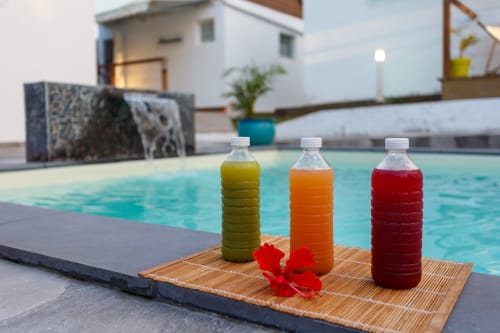 Trois jus colorés au bord de la piscine de Kaz A Bibi, une maison d'hôtes à Sainte-Rose avec eau turquoise et bâtiments blancs