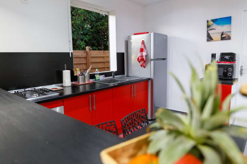 Cuisine moderne rouge et noir à la Kaz A Bibi B&B à Sainte-Rose avec réfrigérateur inox et vue sur le jardin