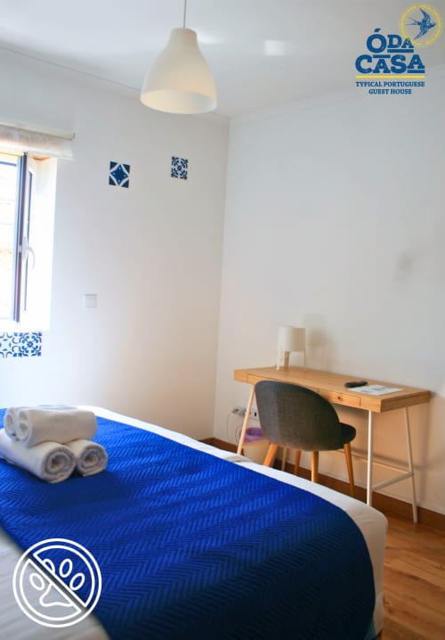 Quarto luminoso na pousada Ó da Casa em Peniche com cama azul, escrivaninha de madeira e detalhes em azulejos azuis portugueses